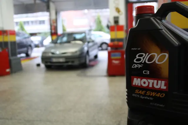 Garrafa de aceite sintético Motul con el taller al fondo
